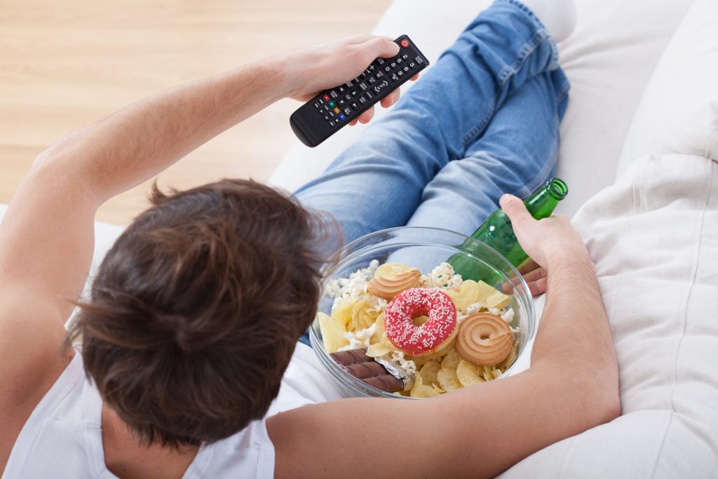 Man watching TV with plate of junk food